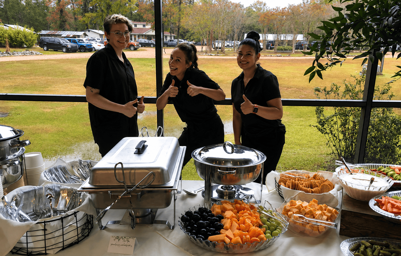 Three servers smiling behind outdoor buffet table